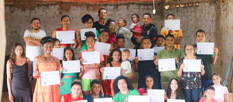 31 personas jóvenes y niños, de pie y cuclillas, en una sala sosteniendo los diplomas obtenidos tras haber completado un taller de comunicación